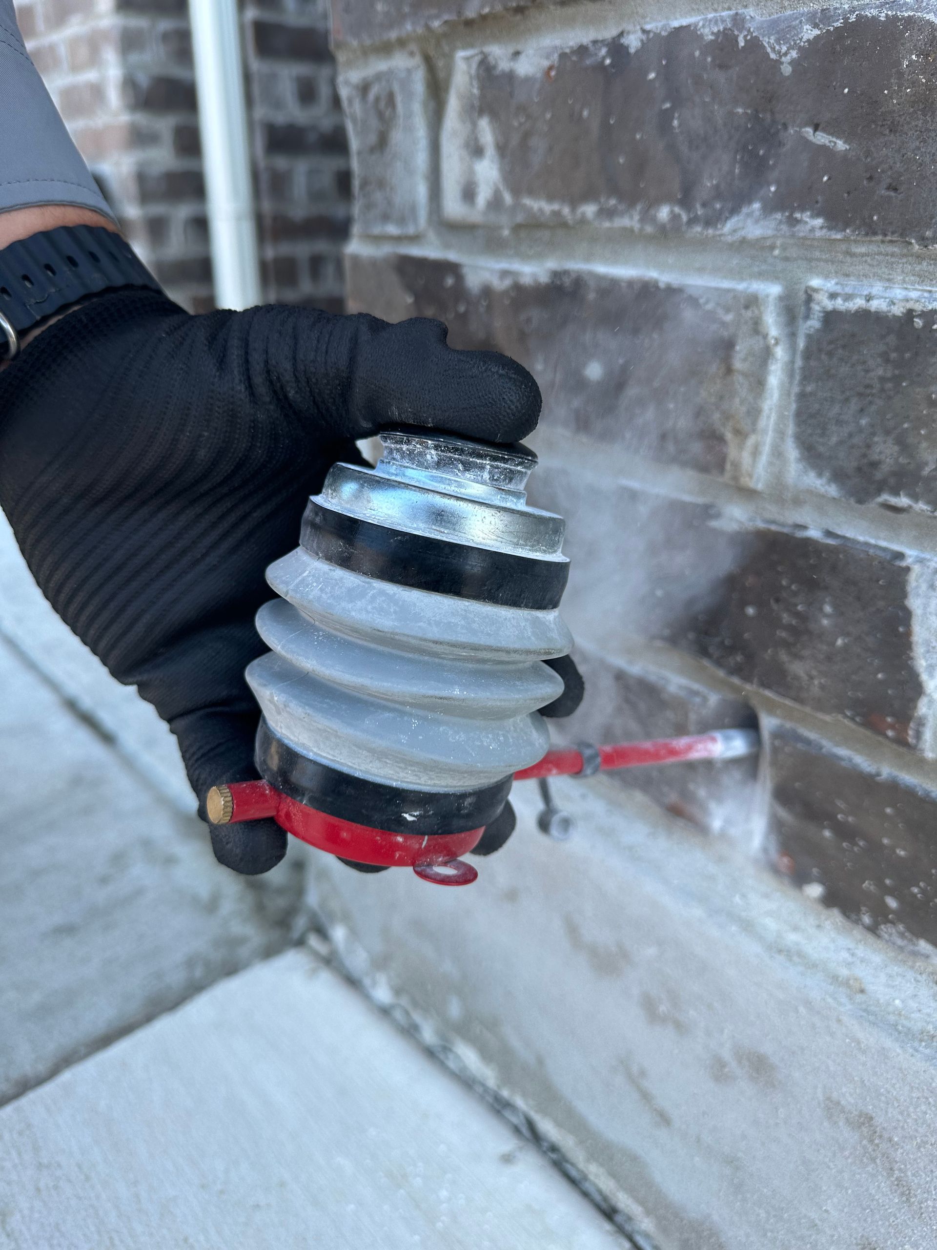 A person in black gloves holding small pest control tool into a brick wall.