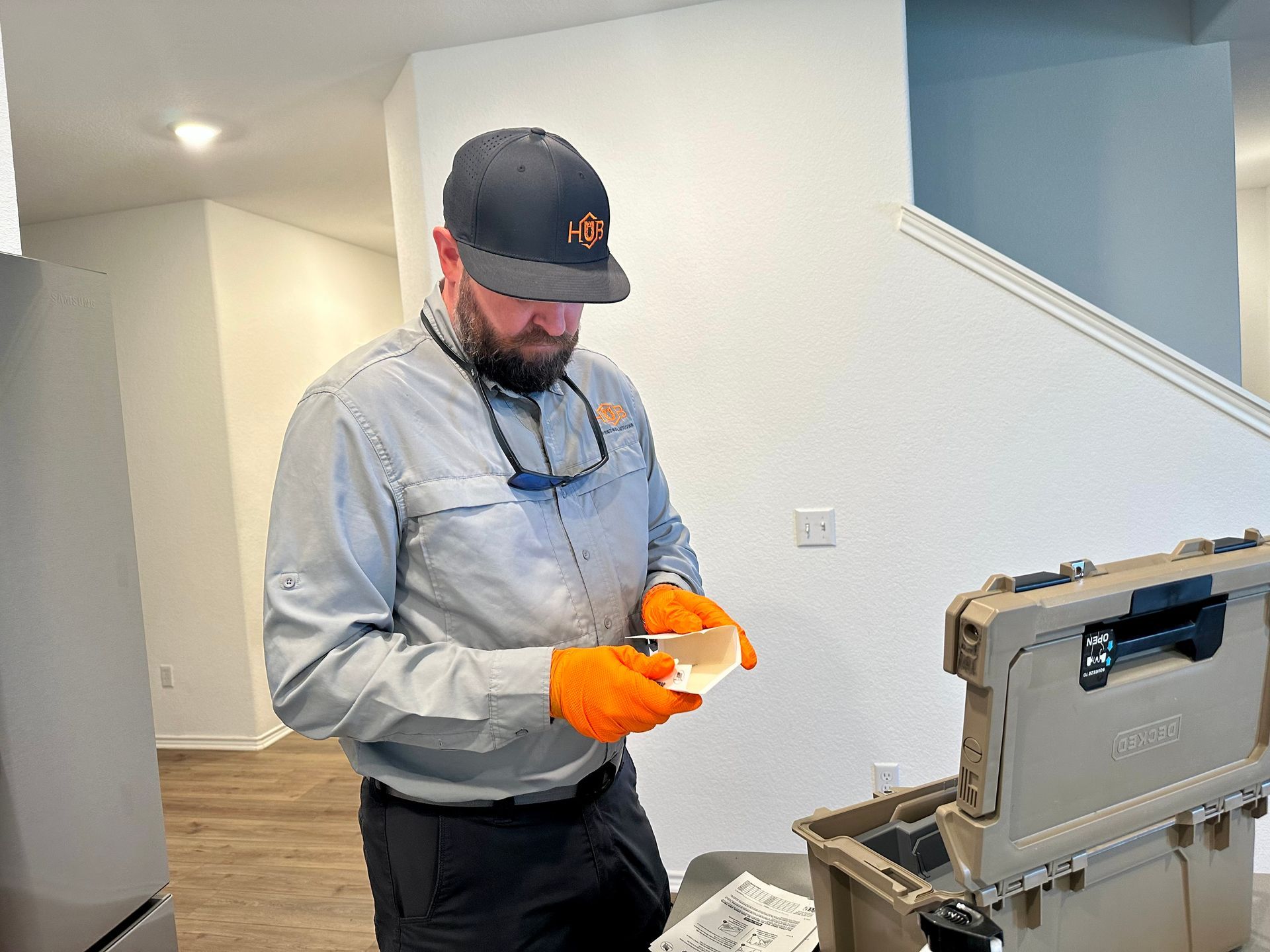 Pest control technician in orange gloves inspecting a sample near an open tool case in a home.