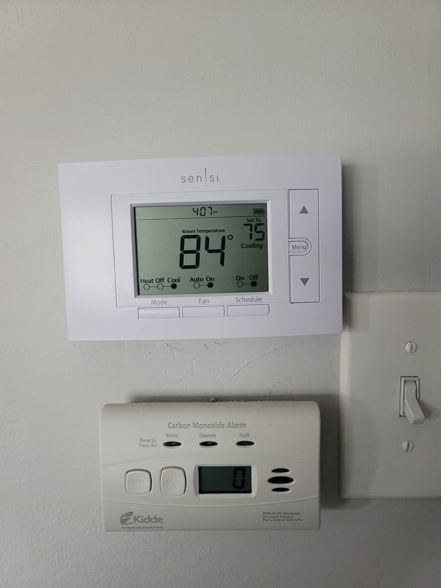 A thermostat is hanging on a wall next to a smoke detector.