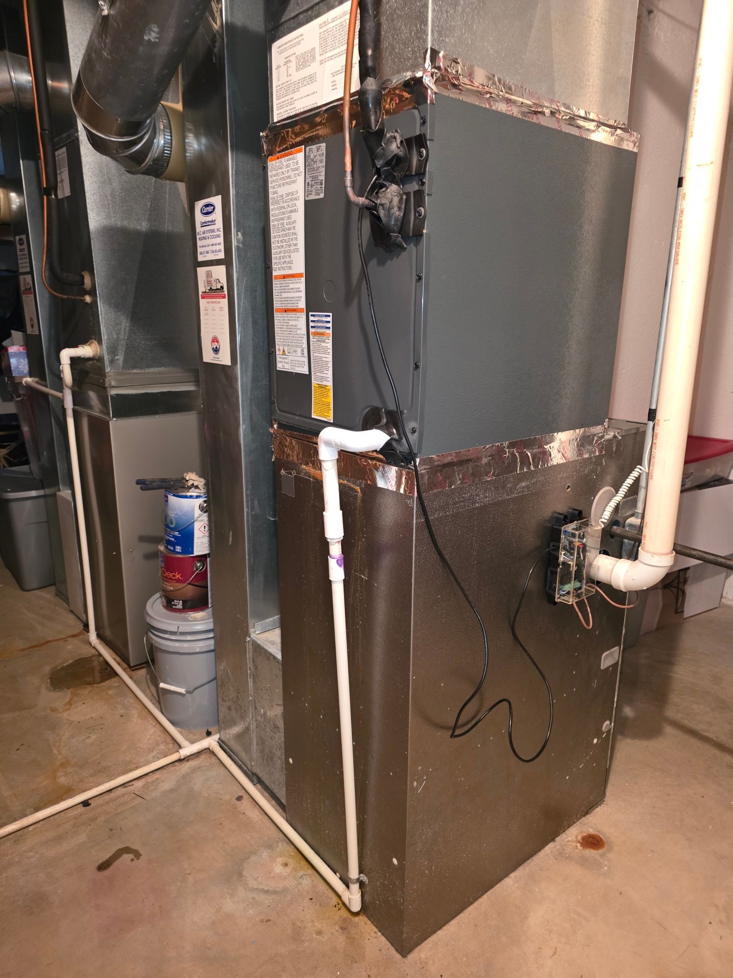 An air conditioner is sitting in a basement next to a pipe.