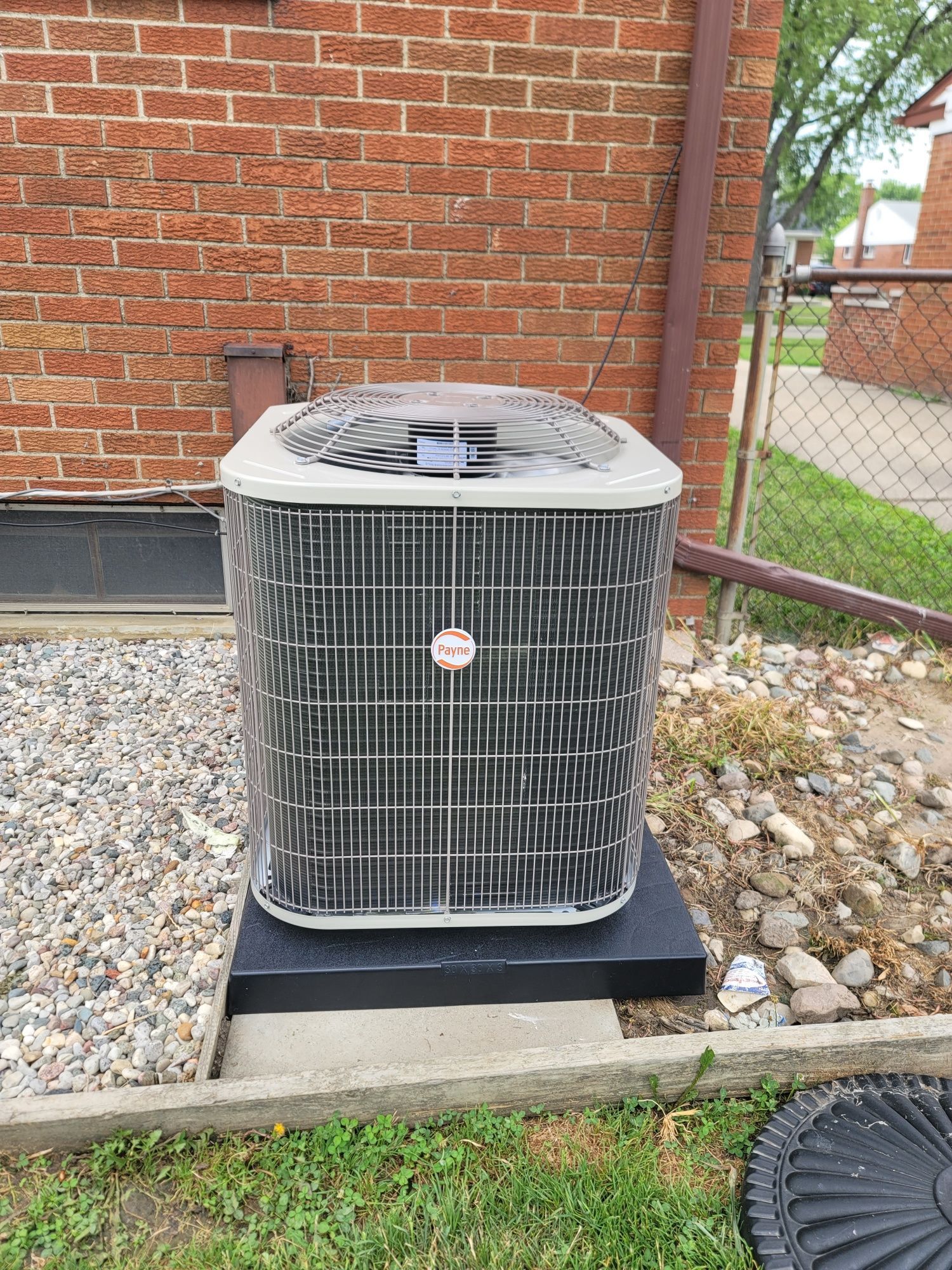 A large air conditioner is sitting outside of a brick building.