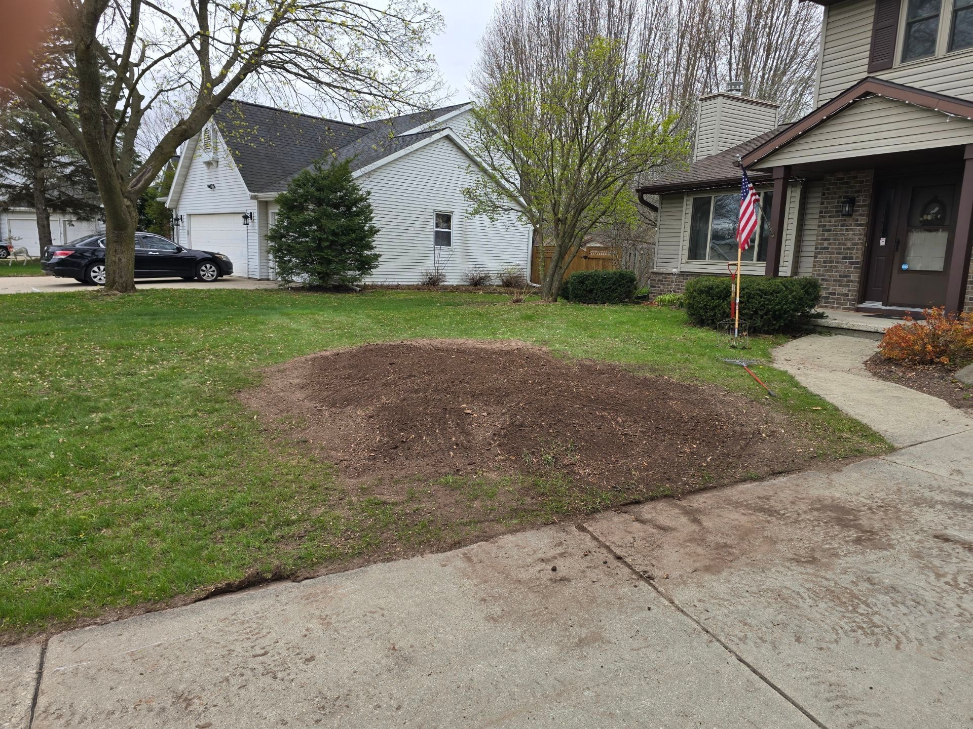 There is a large pile of dirt in the middle of the grass in front of a house.