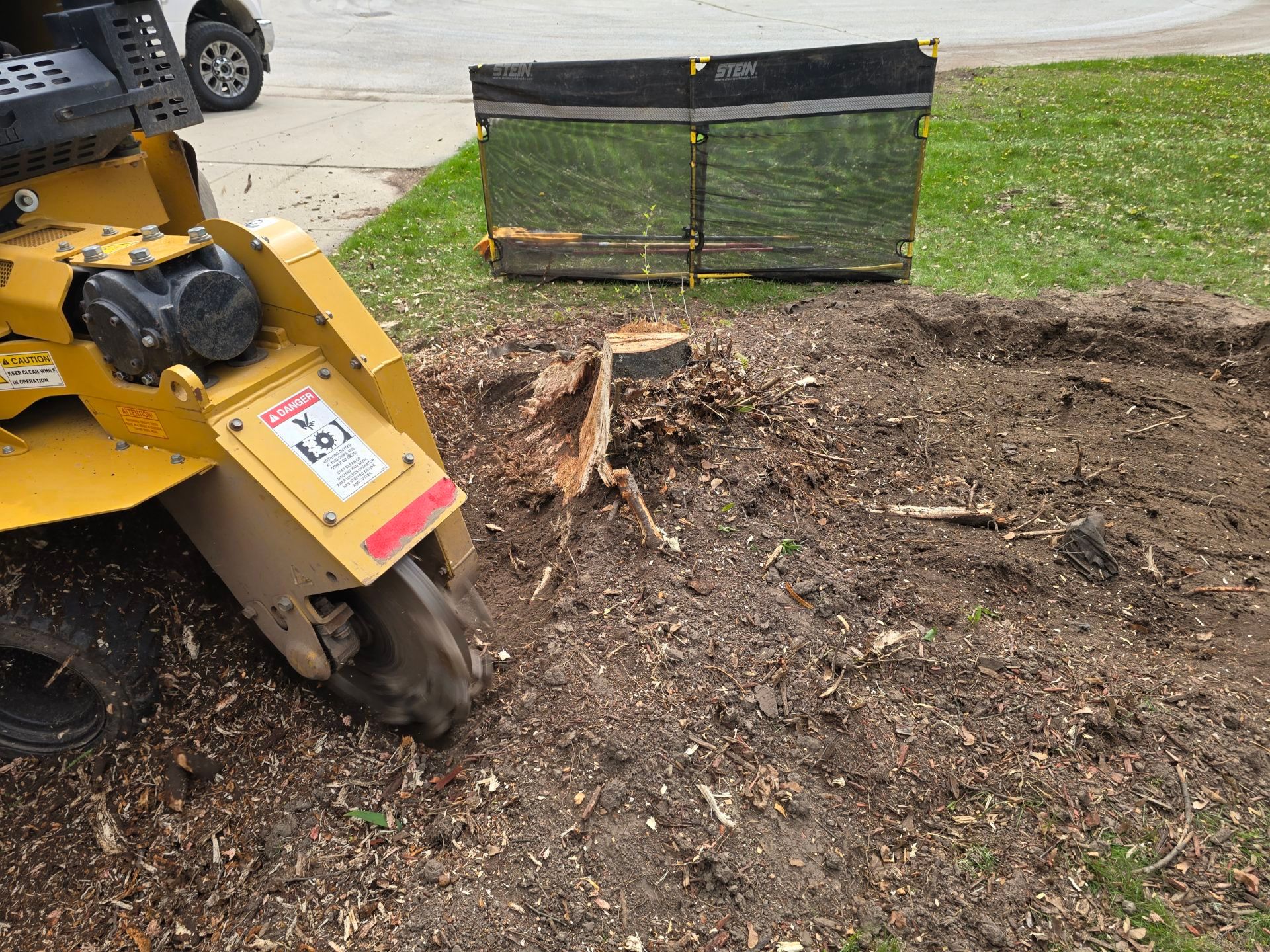A yellow stump grinder is cutting a tree stump in the ground.