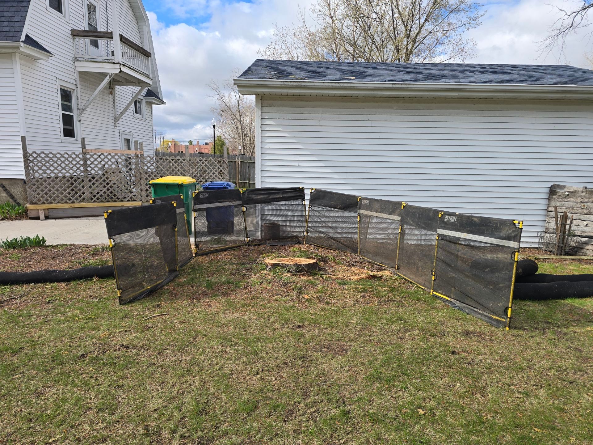 A fence is surrounding a tree stump in the backyard of a house.