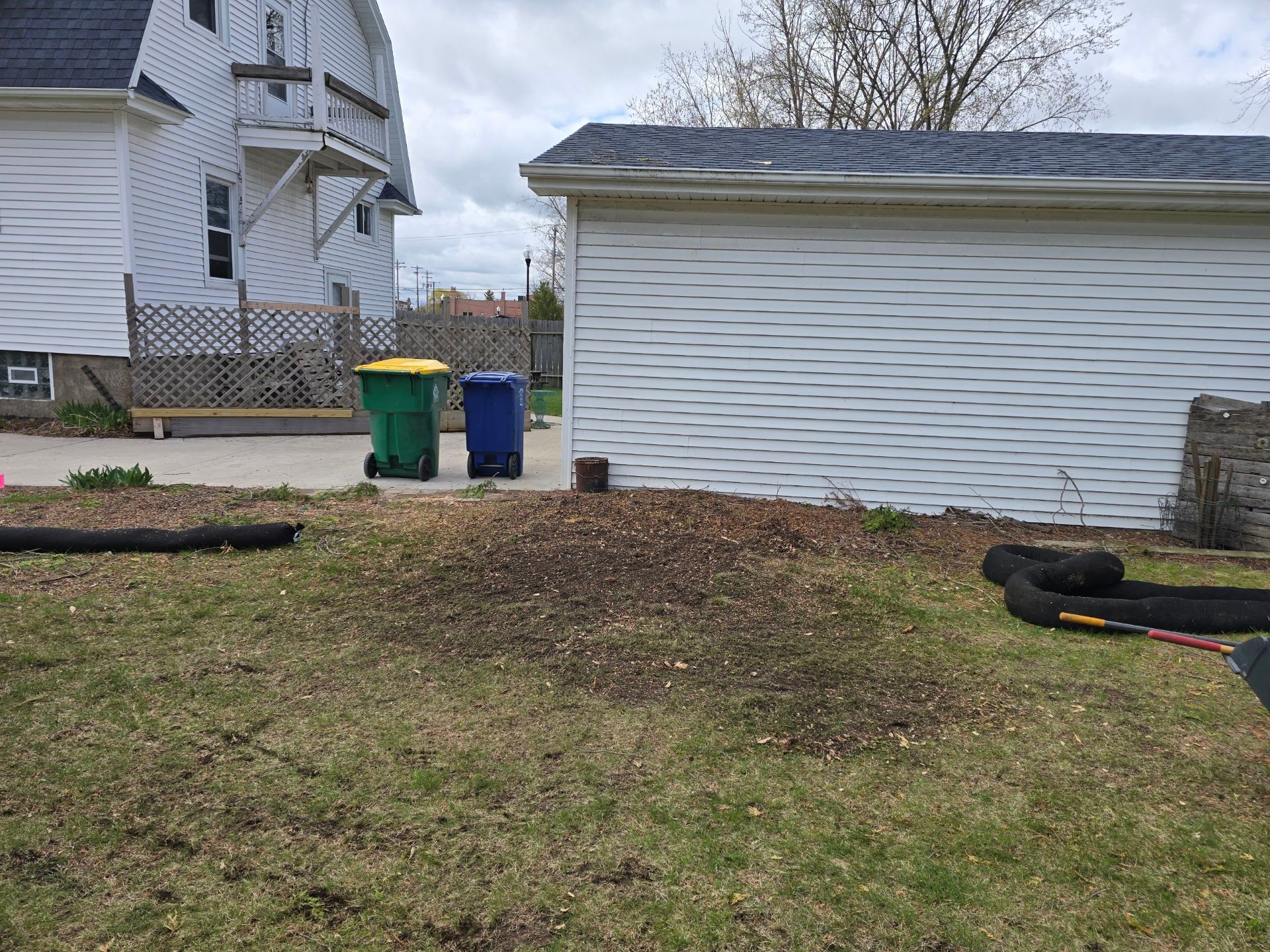 There are three trash cans in the backyard of a house.