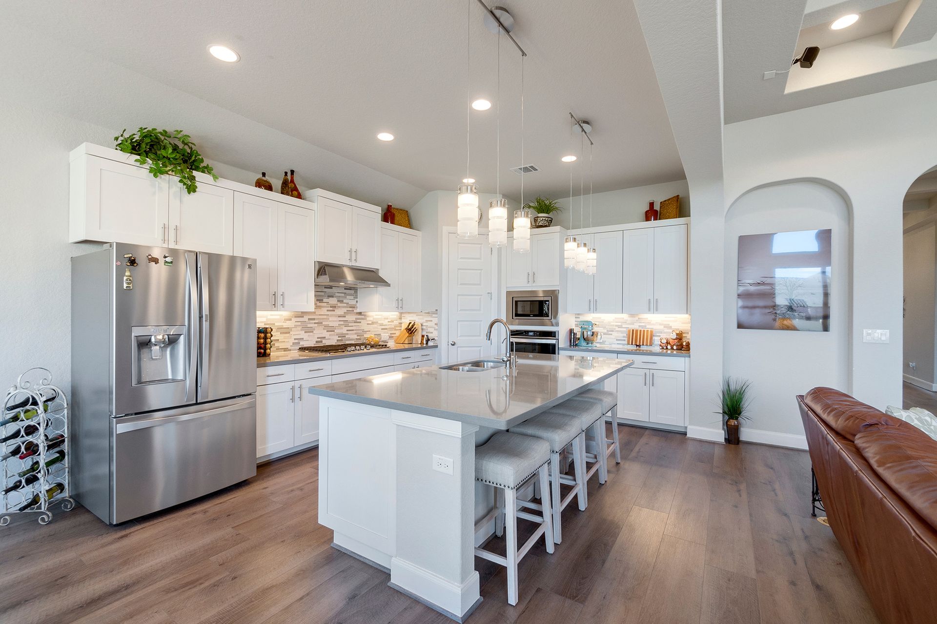 Bright modern kitchen with white cabinets, stainless fridge, island, and bar stools