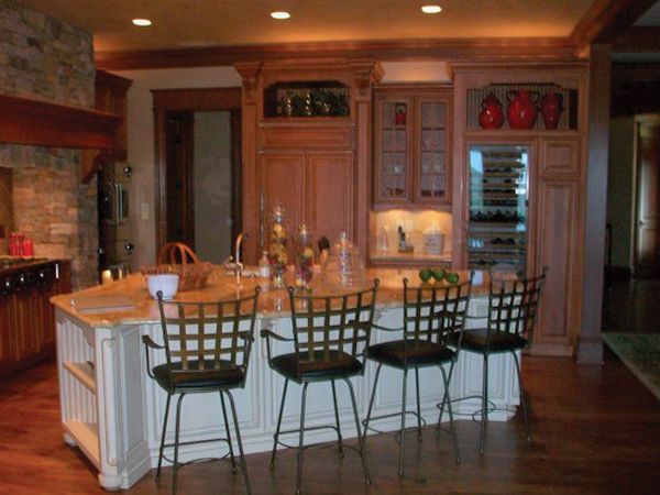 Warm kitchen with wood cabinets, island, black chairs, brick fireplace, and built-in wine cooler.