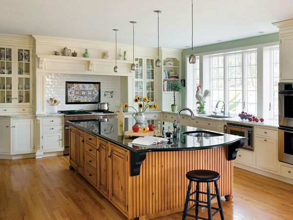 Bright kitchen with wooden island, black countertop, white cabinets, and large sunlit windows