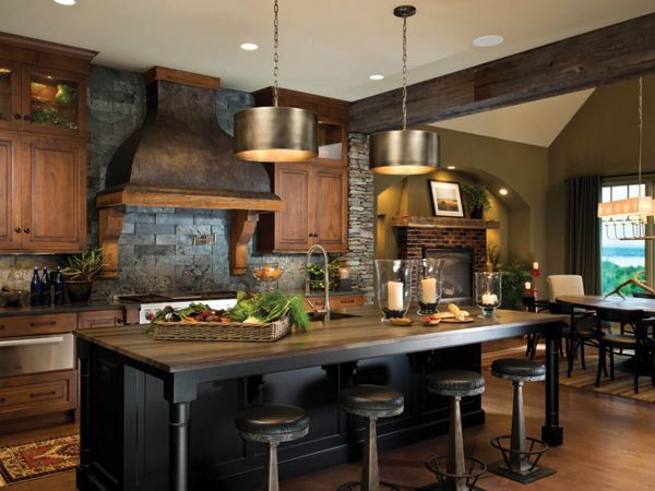 Warm kitchen with dark wood island, stools, stone range hood, and pendant lights