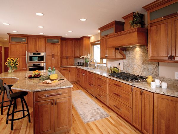 Warm wood kitchen with island, built-in oven, gas range, and fruit on a countertop under recessed lighting
