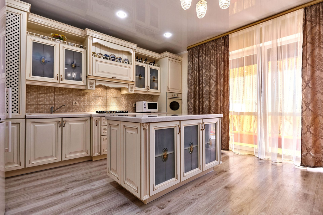 Elegant white kitchen with island, tiled backsplash, and sunlight through sheer curtains.