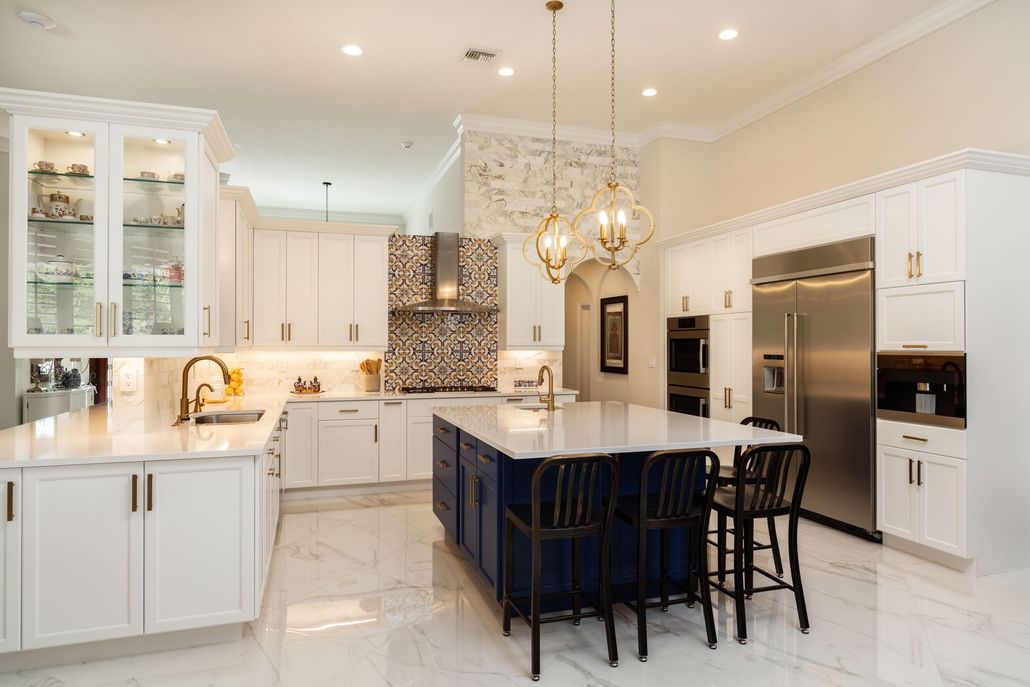 Bright white luxury kitchen with marble island, navy stools, and gold chandeliers