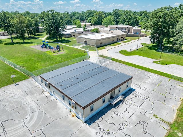 Aerial view of a small building with parking lot, grassy grounds, and trees on a sunny day
