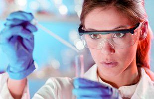 Focused young life science professional pipetting solution into the glass cuvette. Lens focus on the researcher's eye.