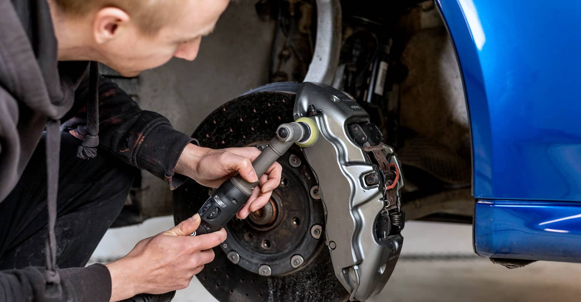 Mechanic working on a car's brake system, using a power tool on a brake caliper.