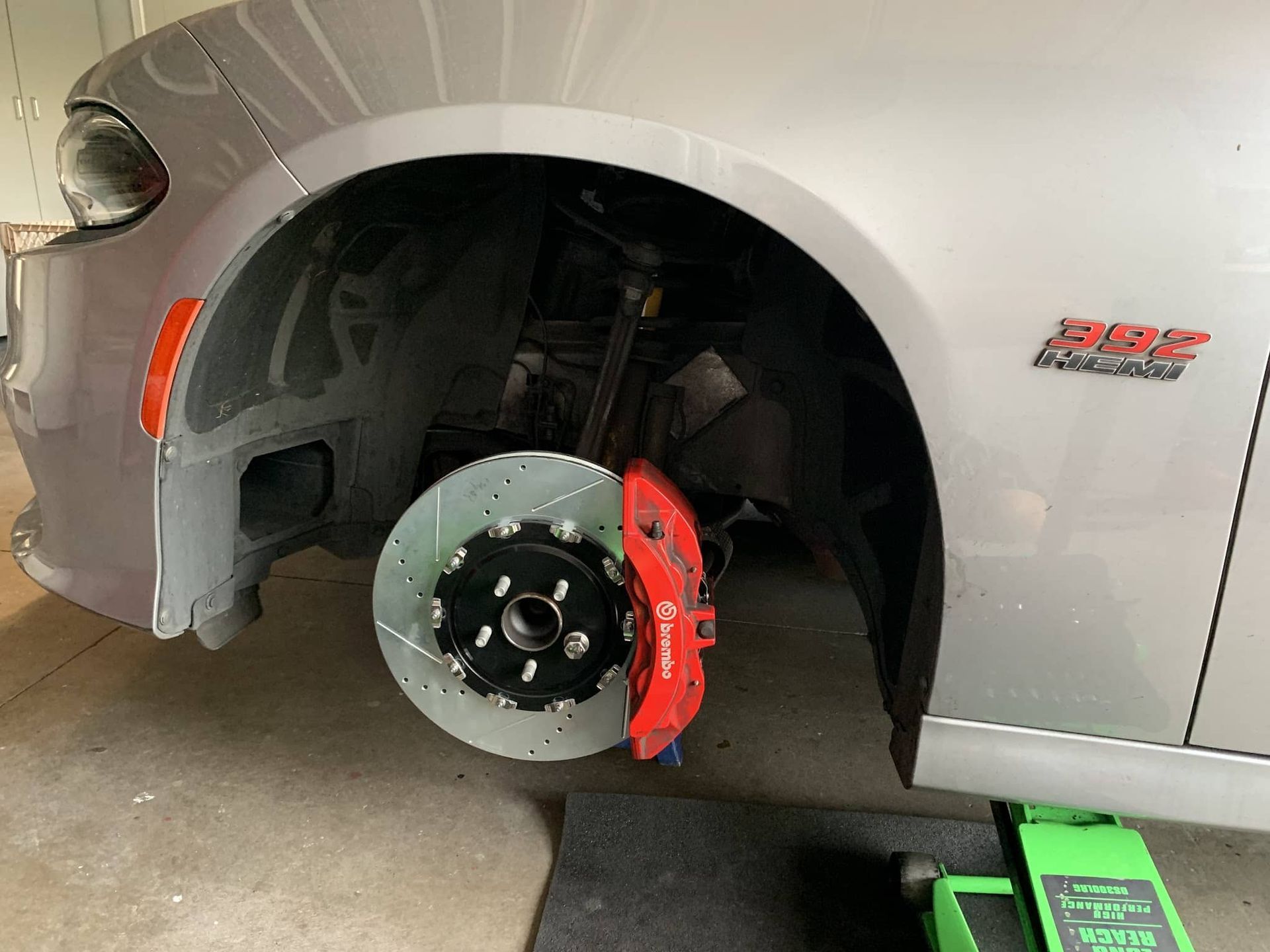 Silver car with front wheel removed, showing red brake caliper and drilled rotor.