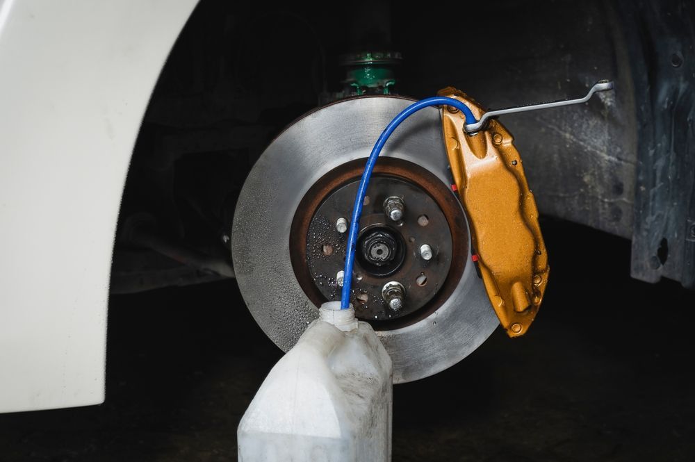 Brake disc assembly with gold caliper and blue tube draining fluid into a container.