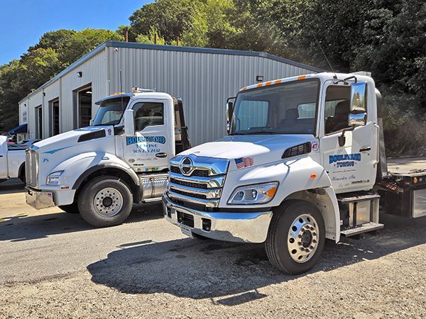 Two white tow trucks parked outside a metal building.