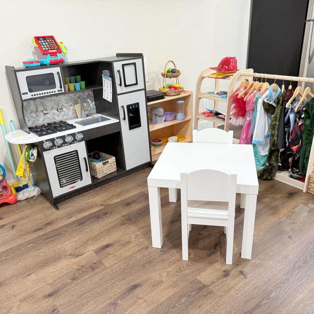 Children’s playroom with toy kitchen, white table and chairs, doll clothes rack, and shelves of toys