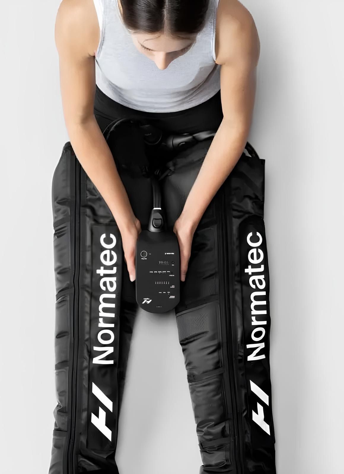 A woman is sitting on the floor wearing a pair of Normatec compression pants.