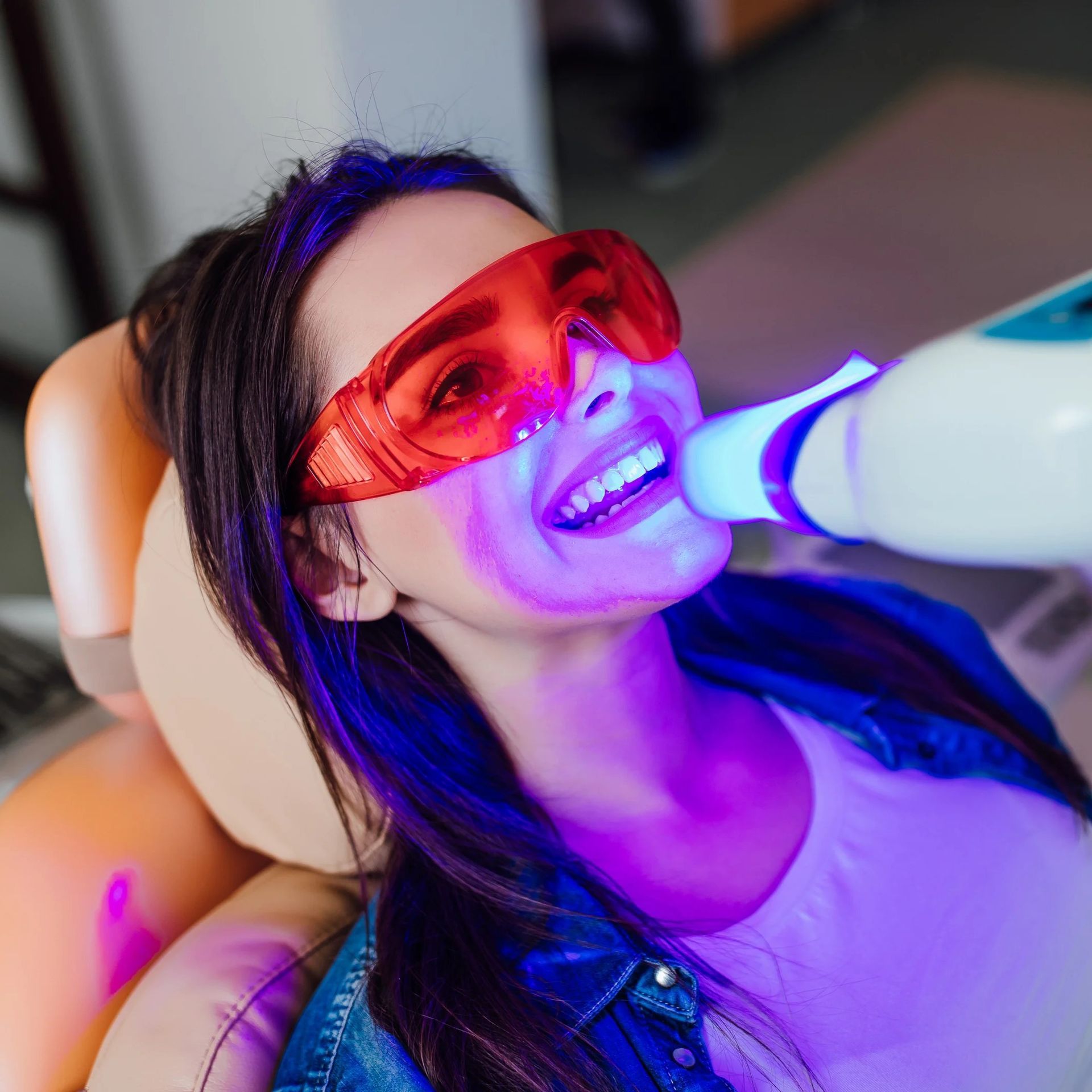 A woman wearing red glasses is smiling while getting her teeth whitened.