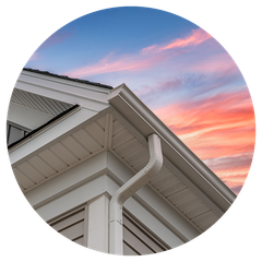 A gutter on the side of a house with a sunset in the background.