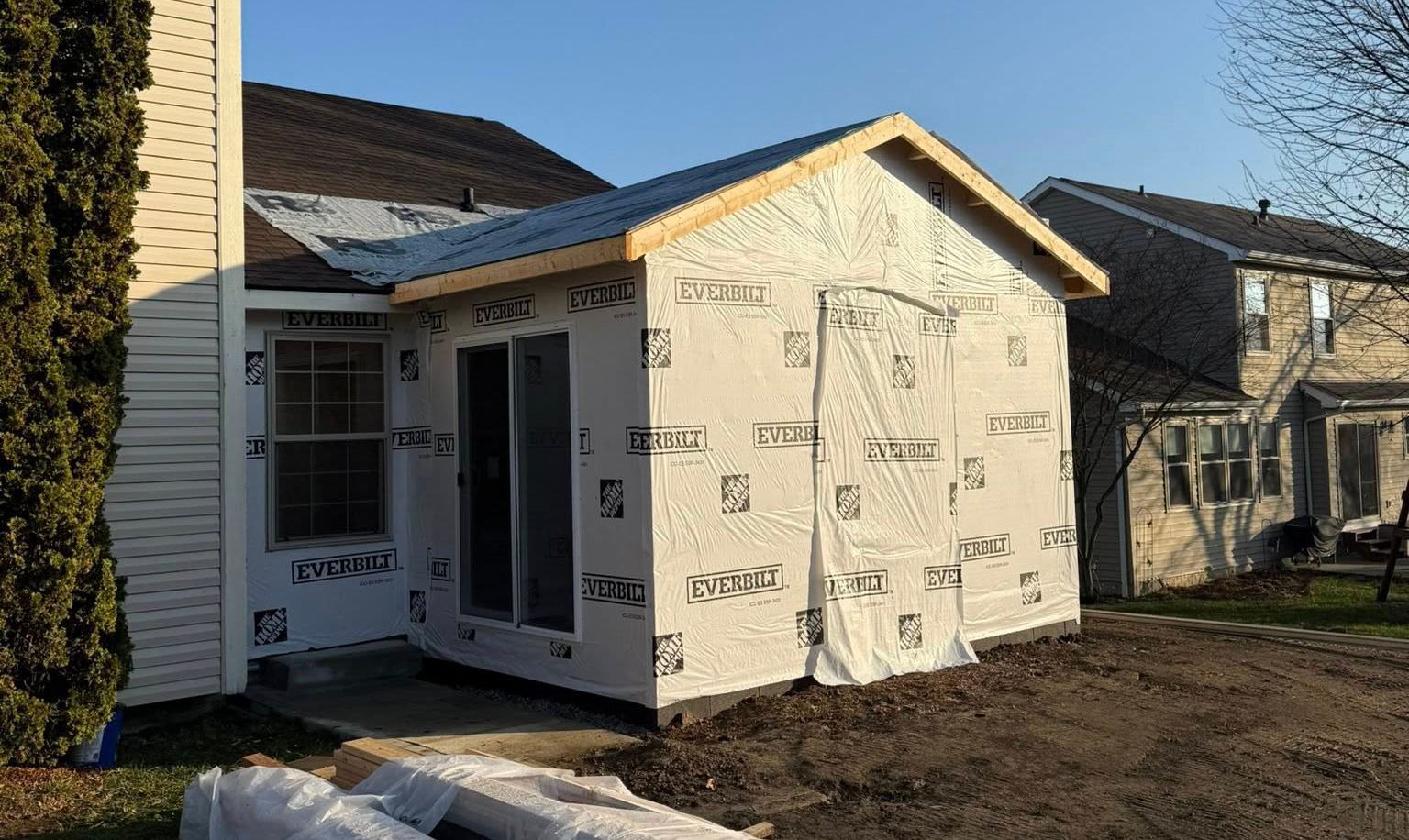 Partially built small house wrapped in house wrap, with unfinished siding and a concrete driveway.