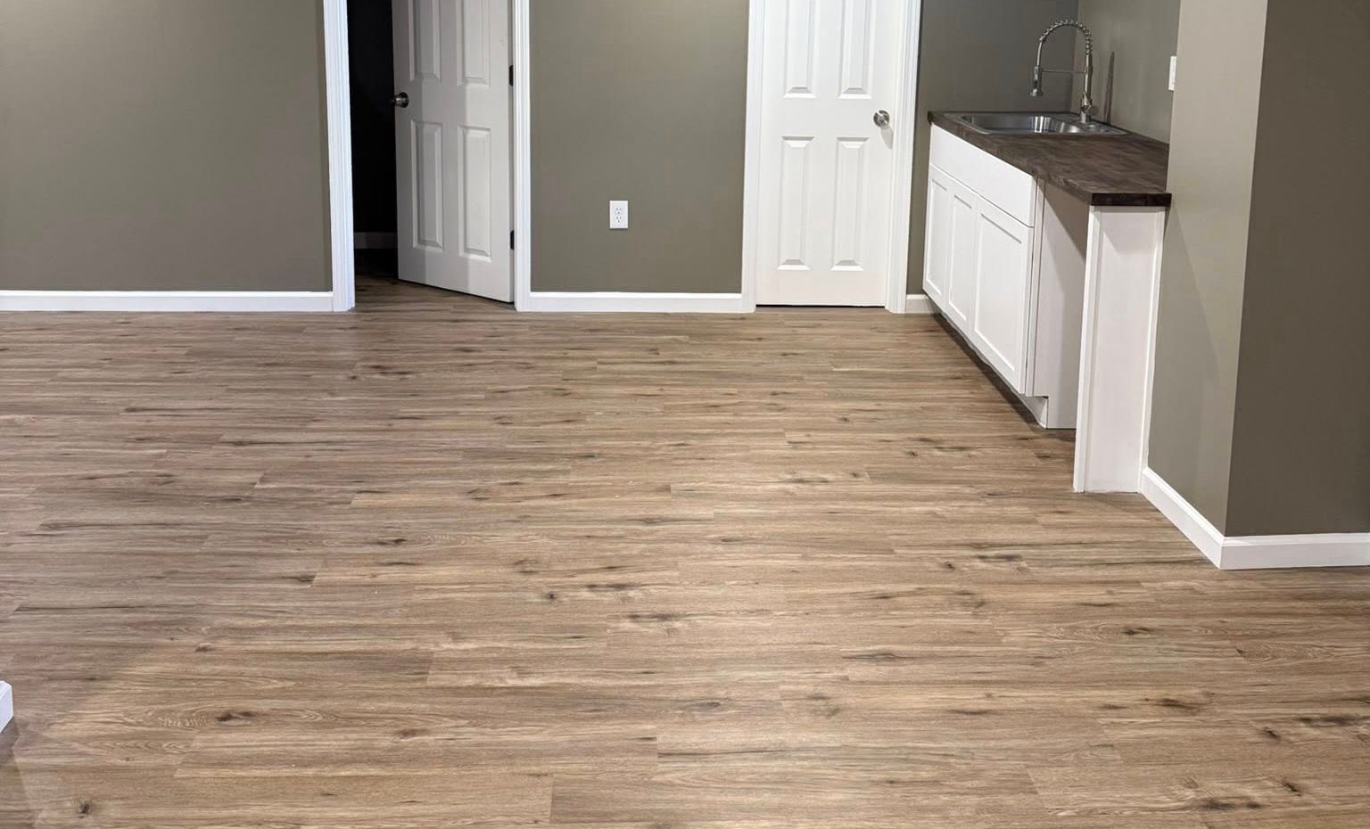 Empty room with wood flooring, gray walls, white doors, and a small kitchenette area.