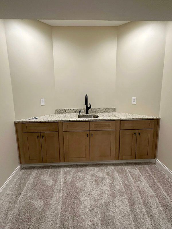 Empty kitchenette with wood cabinets, sink, and beige walls in a carpeted room