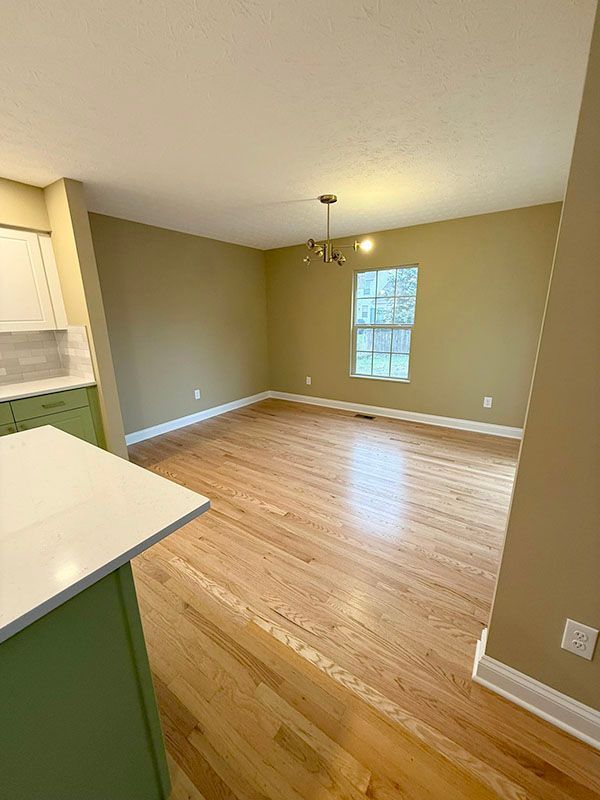 Empty living-dining room with hardwood floors, beige walls, and a ceiling light
