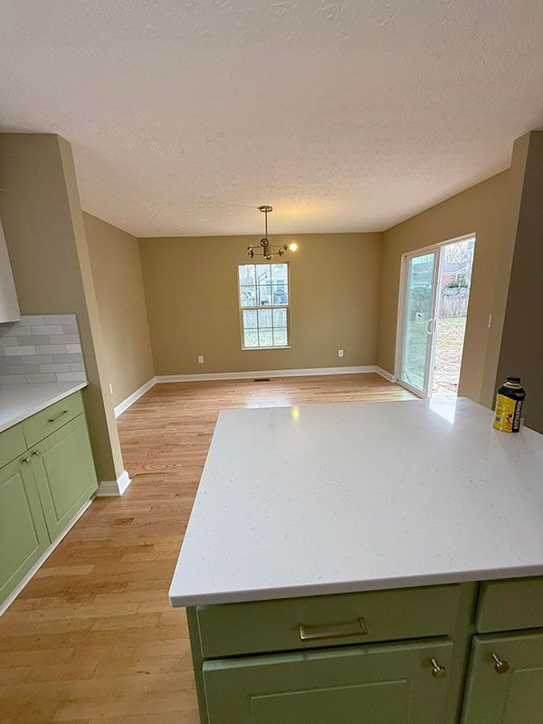 Empty kitchen and dining area with white island, green cabinets, beige walls, and hardwood floor