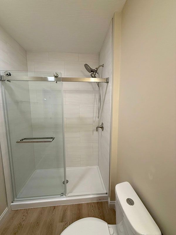 Empty bathroom with glass shower, white tile, wood-look floor, and a white toilet bench