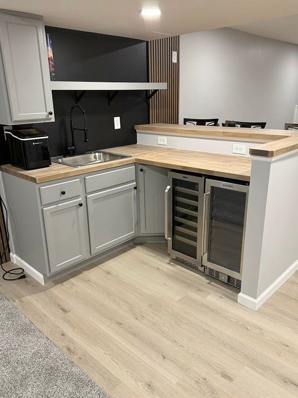 Compact modern kitchen with gray cabinets, wood countertops, and a built-in wine fridge on light flooring