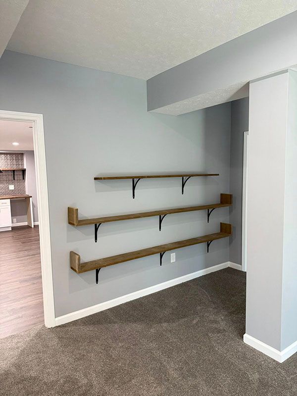 Empty gray room with wall-mounted wooden shelves and carpeted floor