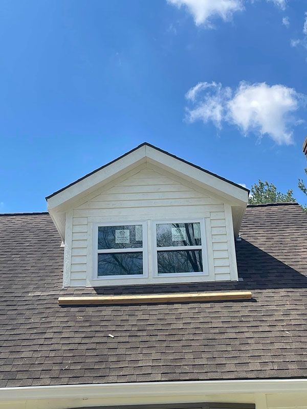 Dormer window with white trim on a shingled roof under a blue sky
