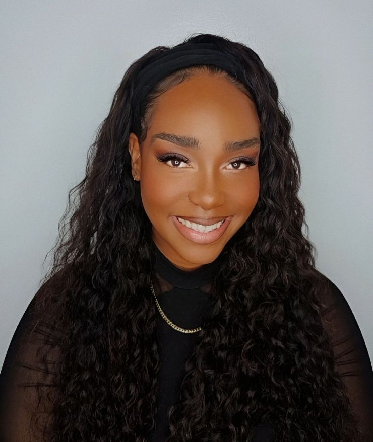 A woman with curly hair is wearing a headband and smiling