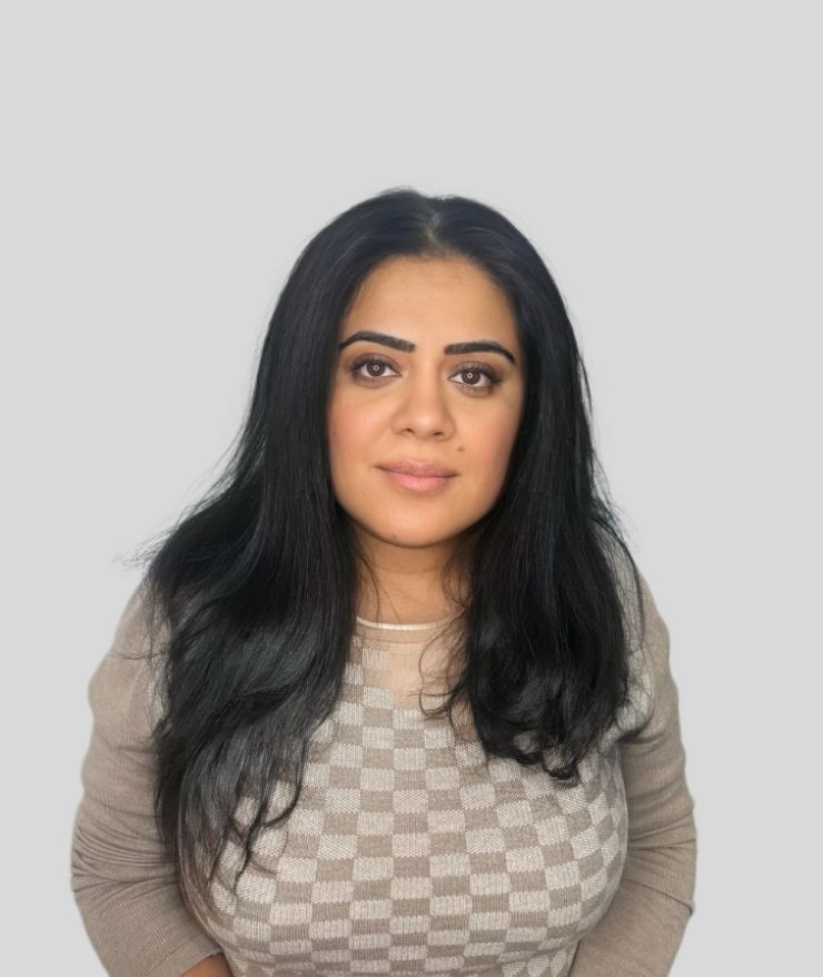 A woman with long black hair is standing in front of a white background.