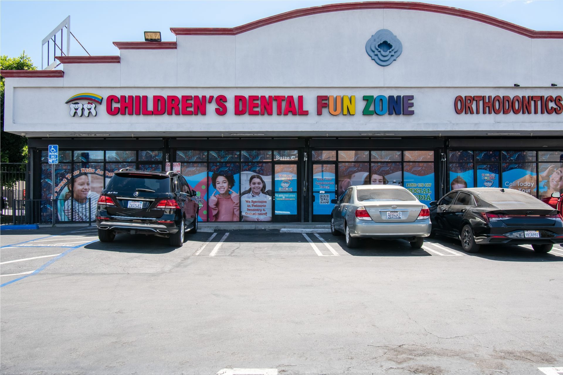 A row of cars are parked in front of a children 's dental fun zone.