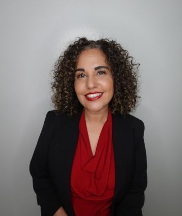 A woman with curly hair is wearing a red shirt and a black jacket.