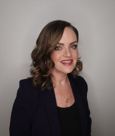 A woman in a blue jacket and black top is smiling for the camera.