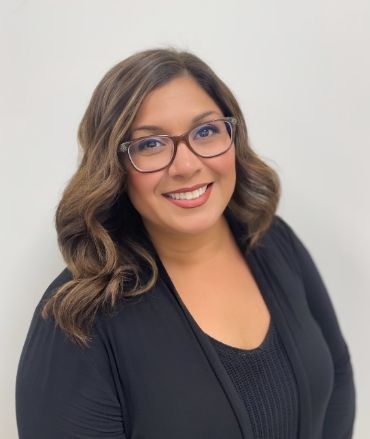 A woman wearing glasses and a black shirt is smiling for the camera.