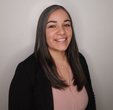 A woman wearing a black jacket and a pink shirt is smiling for the camera.