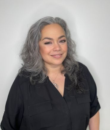 A woman with gray hair and a black shirt is smiling for the camera.