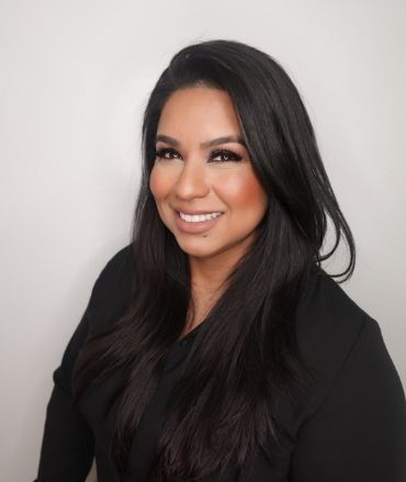 A woman with long dark hair is smiling and wearing a black shirt.