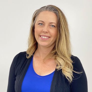 A woman wearing a blue shirt and a black cardigan is smiling for the camera.