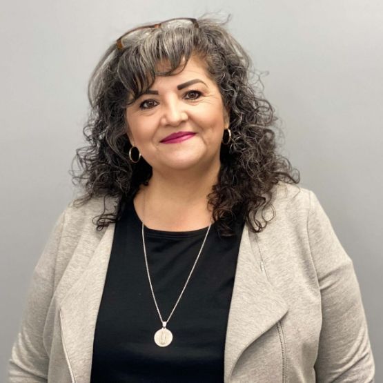 A woman with curly hair is wearing a black shirt and a grey jacket.