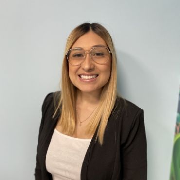 A woman wearing glasses and a black jacket is smiling for the camera.