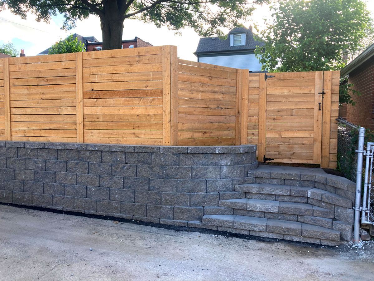 Stone retaining wall beneath a wooden fence in a wooded yard