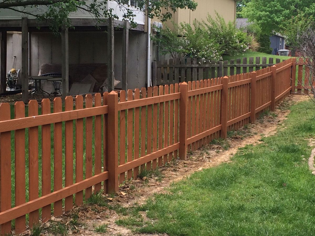 Brown wooden fence along a grassy yard beside a house and patio.