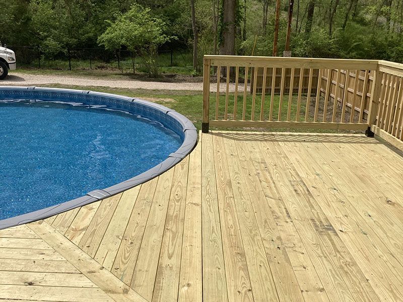 Wooden deck beside a blue swimming pool with a railing and trees in the background